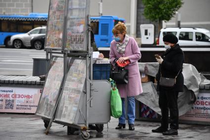 Москва.  Женщина в медицинской маске покупает газету.