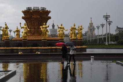 Москва.  Прохожие гуляют у фонтана `Дружба народов`на ВДНХ во время дождя.