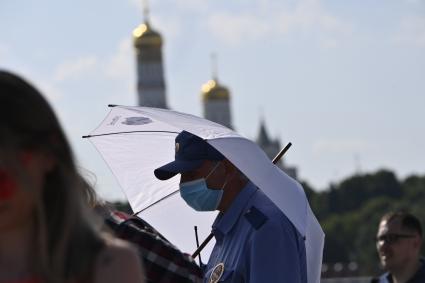 Москва. Мужчина под зонтом в медицинской маске в парке Зарядье.