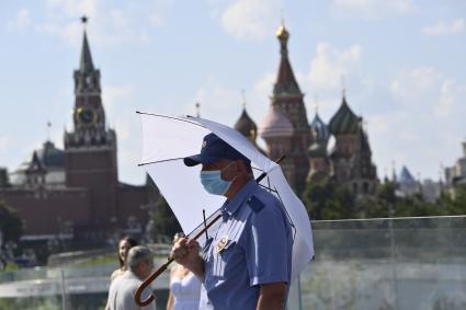 Москва. Мужчина под зонтом в медицинской маске в парке Зарядье.