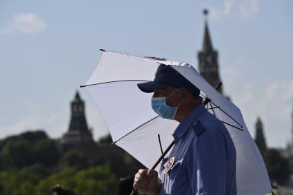 Москва. Мужчина под зонтом в медицинской маске в парке Зарядье.