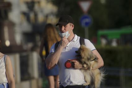 Екатеринбург. Мужчина в медицинской маске с собачкой на руках на набережной реки Исеть во время летней жары