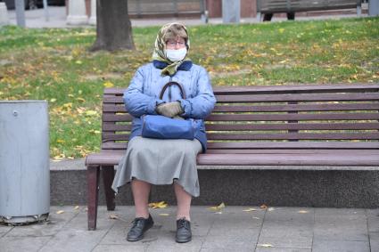 Москва.  Женщина в медицинской маске сидит на скамейке.