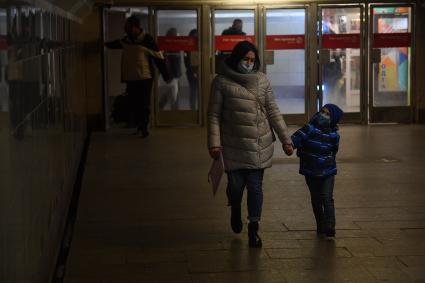 Москва. Женщина с ребенком в медицинских масках в подземном переходе метро.