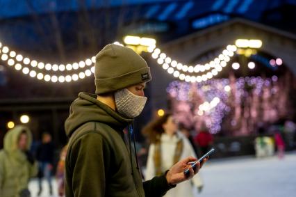 Санкт-Петербург.  Молодой человек в защитной маске с мобильным телефоном руке.