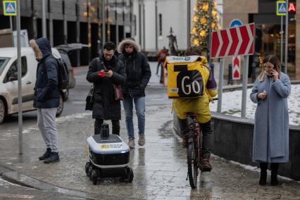 Москва.  Курьер службы доставки `Яндекс Go` и робот-доставщик еды `Яндекс.Ровер`.