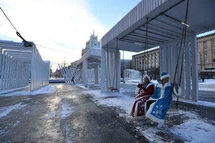 Москва.   Мужчина и женщина в костюмах деда Мороза и Снегурочки на качелях на Триумфальной площади.