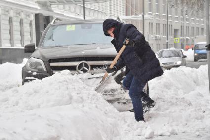 Москва. Мужчина расчищает дорогу возле автомобиля после снегопада.