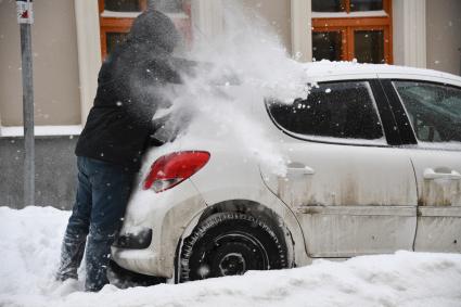 Москва. Водитель счищает снег с машины.