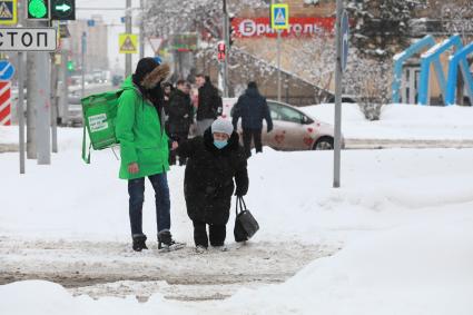 Красноярск. Юноша помогает пожилой женщине перейти дорогу, неубранную от снега.