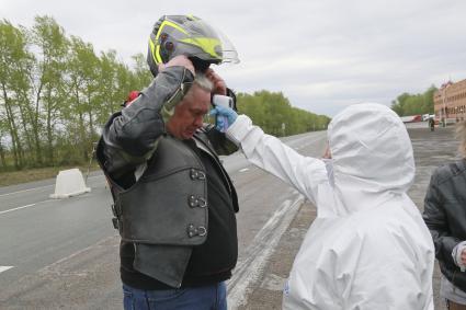 Барнаул. Сотрудник Роспотребнадзора измеряет температуру мотоциклисту во время проверки пропусков на выезде из города. С 1 мая действует пропускной режим в связи с введением ограничений из-за распространения COVID-19.