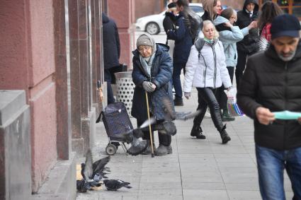 Москва. Пожилая женщина стоит на улице и смотрит на голубей.