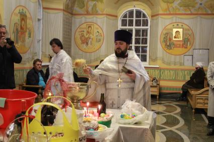 Иркутск.  Священнослужитель освящает пасхальные куличи и яйца.