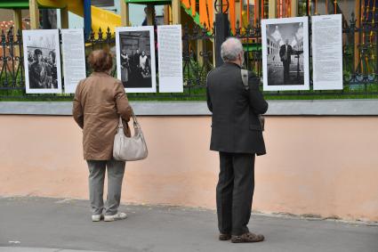 Москва.  Прохожие у фотографий  на выставке под открытым небом -  проект `Люди` журналиста и фотографа Юрия Роста , у храма Живоначальной Троицы в Хохлах .