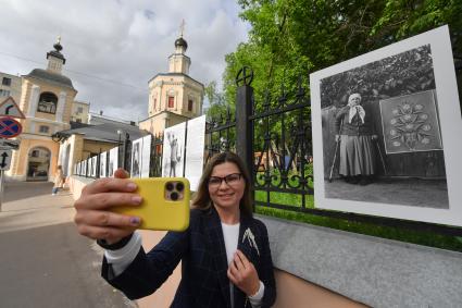 Москва.  Прохожие у фотографий  на выставке под открытым небом -  проект `Люди` журналиста и фотографа Юрия Роста , у храма Живоначальной Троицы в Хохлах .