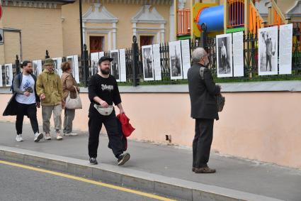 Москва.  Прохожие у фотографий  на выставке под открытым небом -  проект `Люди` журналиста и фотографа Юрия Роста , у храма Живоначальной Троицы в Хохлах .