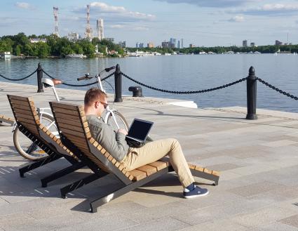 Москва. Мужчина с ноутбуком сидит на лежаке пляжной зоны возле Северного речного вокзала у Химкинского водохранилища.