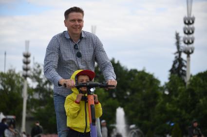 Москва. Мужчина с мальчиком едет на электросамокате на ВДНХ.