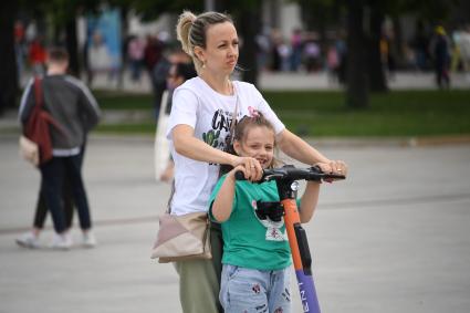 Москва.   Женщина с девочкой на самокате.