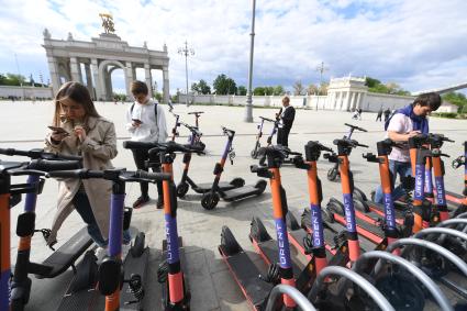 Москва.  Посетители берут самокаты на пункте проката электросамокатов на ВДНХ.