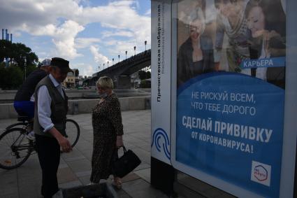 Москва. Мужчина и женщина у плаката с призывом сделать прививку.
