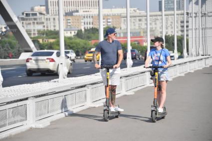 Москва. Мужчина и девушка на самокатах на Крымском мосту.