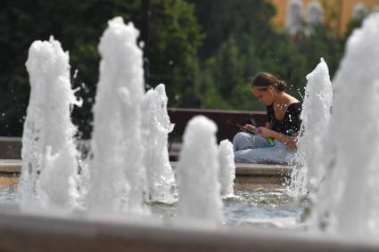 Москва. Девушка с мобильным телефоном и бутылкой минеральной воды сидит у фонтана.