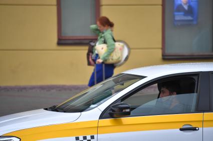 Москва. Девушка с багажом идет по улице, рядом стоит такси.