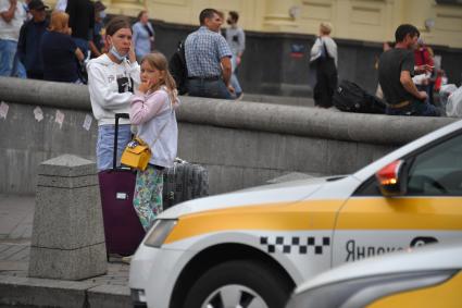 Москва. Женщина и девочка с багажом стоят на тротуаре у такси.