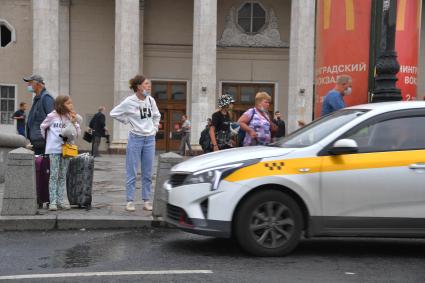 Москва. Женщина и девочка с багажом стоят на тротуаре у такси.