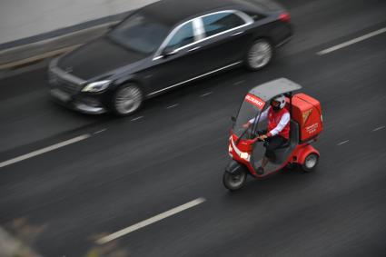 Москва. Курьер `Тануки` едут на скутере по дороге.