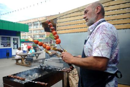 Санкт-Петербург. Южный рынок. Шашлычник жарит мясо и овощи на мангале.