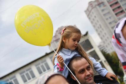 Москва. Первое сентября. Первоклассница держит в руках шарик `Привет, школа!` и сидит на плечах у папы во время торжественной линейке у школы.