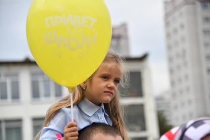 Москва. Первое сентября. Первоклассница держит в руках шарик `Привет, школа!` и сидит на плечах у папы во время торжественной линейке у школы.