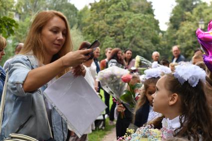 Москва. Первое сентября. Мама фотографирует первоклассницу на торжественной линейке у школы.