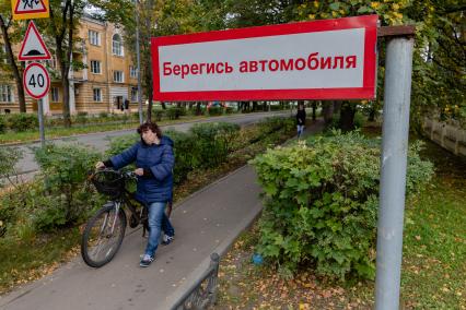 Москва. п.Акулово. Местная жительница катит велосипед рядом с табличкой `Берегись автомобиля`.