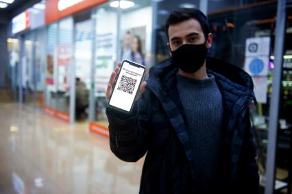 Санкт-Петербург. Юноша в маске и мобильным телефоном, на экране которого отображен QR-код, заходит в торговый центр.