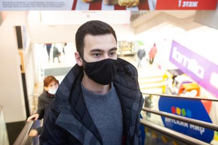Санкт-Петербург. Юноша в защитной маске едет на эскалаторе в торговом центре.