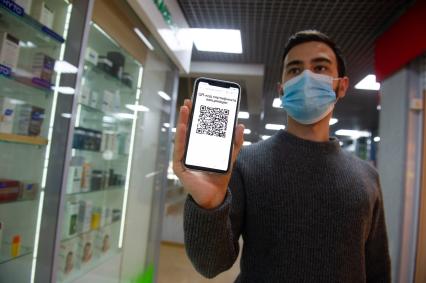 Санкт-Петербург. Юноша с мобильный телефоном, на экране которого отображен QR-код, идет по торговому центру.