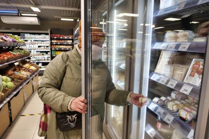 Самара. Женщина достает из холодильника пирожное макаронс в продуктовом магазине.