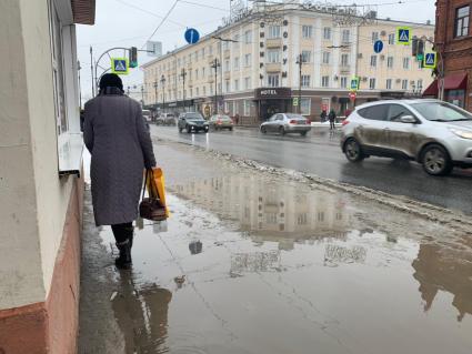 Томск. Женщина обходит большую лужу на тротуаре.