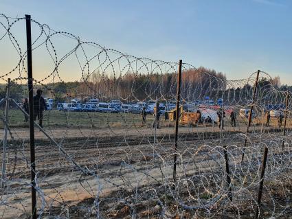 Белорусско-польская граница. Польские полицейские автомобили стоят по другую сторону от лагеря нелегальных мигрантов, где находятся беженцы из Ближнего Востока.