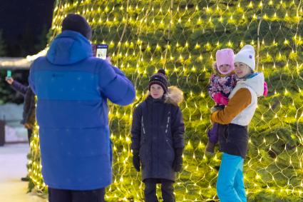 Красноярск. Мужчина и женщина с детьми фотографируются у новогодней елки.