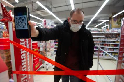 Санкт-Петербург. Мужчина демонстирует QR-код на экране мобильного телефона при входе в продуктовый магазин.