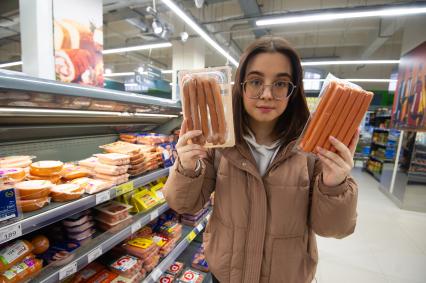 Санкт-Петербург. Девушка выбирает сосиски в продуктовом магазине.