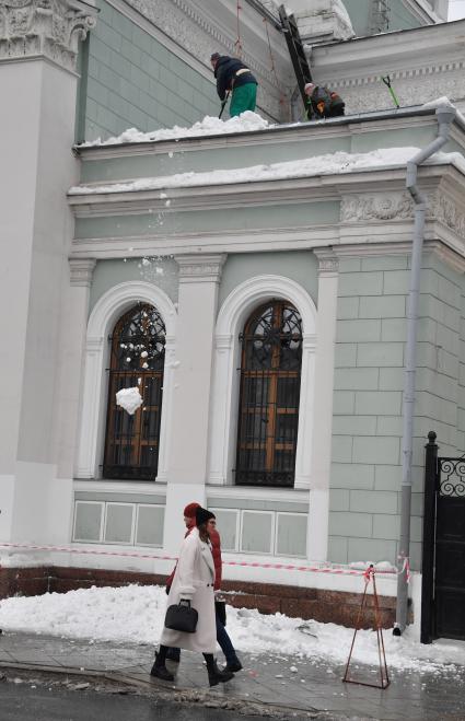 Москва.   Сотрудники коммунальных служб счищают снег с крыши дома.