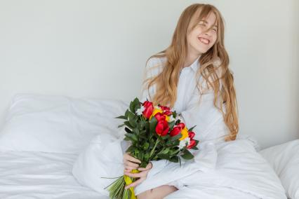 Красноярск. Девушка радуется букету цветов, лежа в постели.