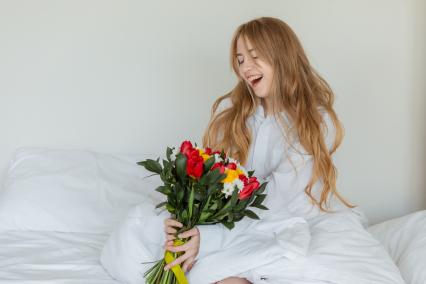 Красноярск. Девушка радуется букету цветов, лежа в постели.