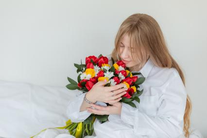 Красноярск. Девушка держит в руках букет цветов, лежа в постели.