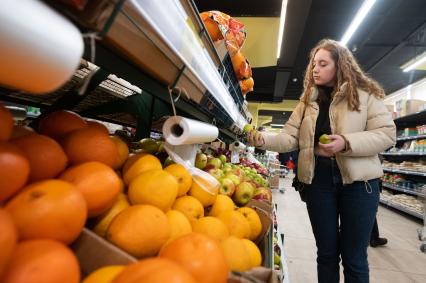 Санкт-Петербург. Девушка выбирает яблоки в продуктовом магазине.